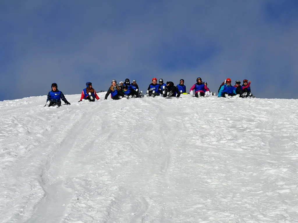 Skigruppe sitzt auf einer Schneekuppe gegen den Himmel.